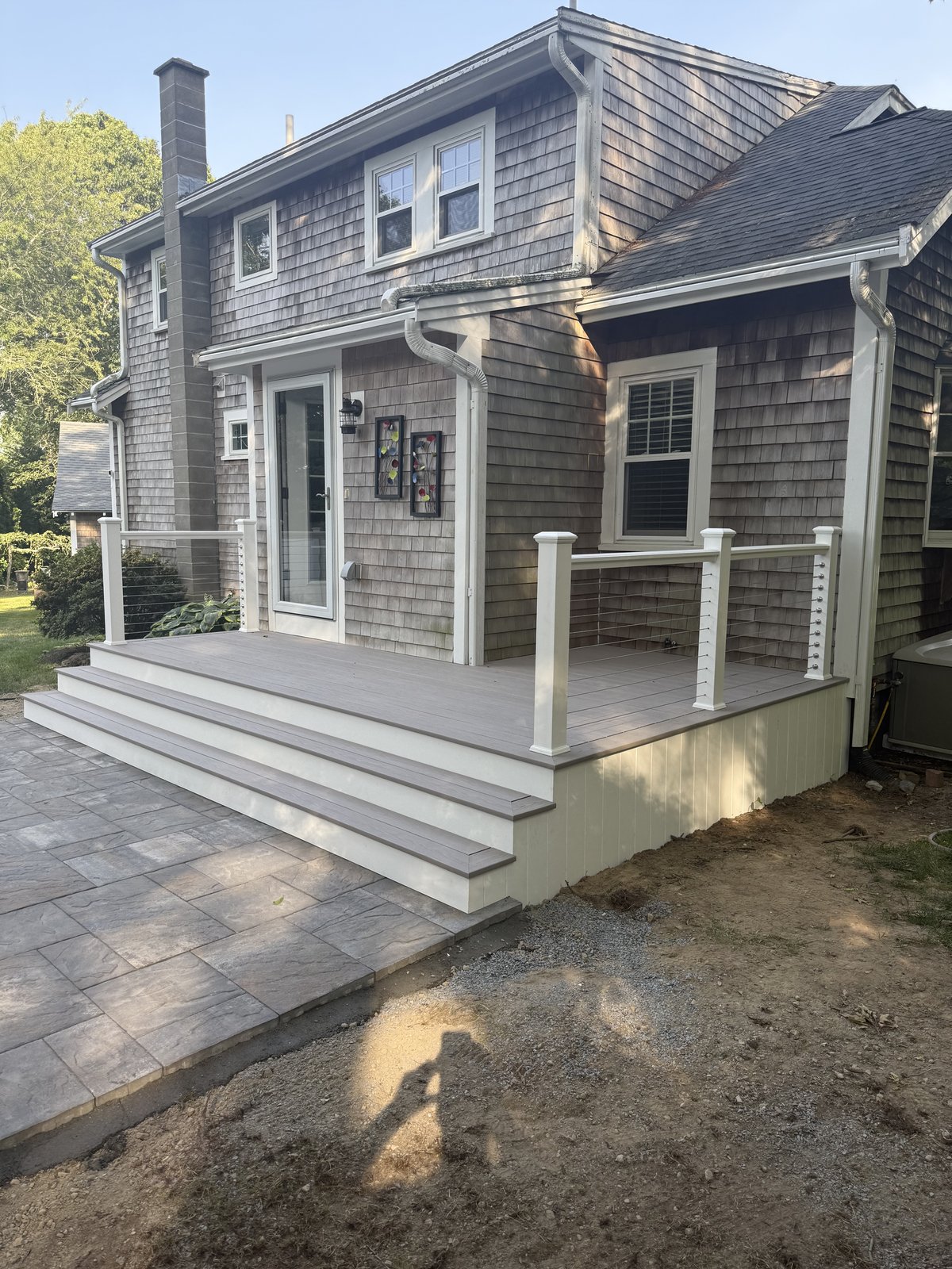 Wraparound farmers porch with composite decking, white columns, and paver landing by Perocchi Building & Remodeling, South Shore MA